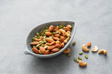 Fındık karışımı. Badem, kaju ve kabak tohumları gri arka planda bir kasede. Sağlıklı enerji atıştırmalığı konsepti. Boşluğu kopyala.