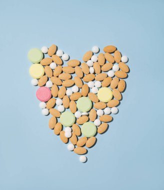 Çeşitli haplar, vitaminler ve mavi arka planda kalp şeklinde farklı renklerde besin takviyeleri. Sağlık hekimi konsepti. Üst görünüm ve kopyalama alanı.