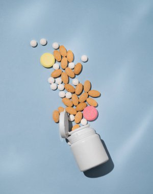 Çeşitli tabletler ve farklı renklerde besin maddeleri açık mavi arkaplandaki beyaz bir şişeden dinamik bir şekilde dökülür. Sağlık hekimi konsepti. Üst görünüm ve kopyalama alanı. 