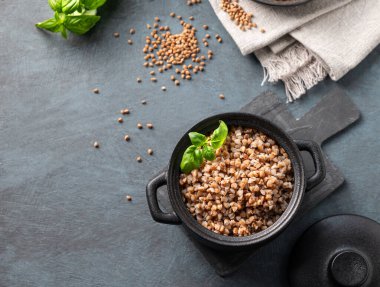 Kara arka planda siyah bir tavada çiğ tahıl ve bitkilerle karabuğday lapası. Doğal, besleyici ve konforlu yiyecek konsepti. Üst görünüm ve kopyalama alanı.