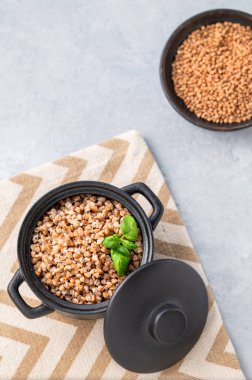 Karabuğday lapası ve siyah bir tavada taze otlar. Arka planda hafif bir arkaplanda ve kuru tahıllar var. Doğal ve besleyici gıda kavramı. Üst görünüm ve kopyalama alanı.