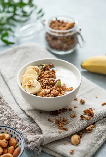 Homemade granola with yogurt, banana and nuts in a bowl on a blue background with dry crynchy and branch. The concept of comfort food and healthy dietary breakfast with a plate of superfood.