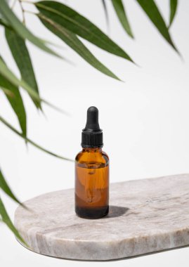 Beyaz arka planda, yaprakları ve gölgesi olan mermer bir tahtanın üzerinde şişedeki yüz ve vücut serumu. Sağlık ve güzellik ürünleri sunumu, satış veya kozmetik reklam afişi için sahne kavramı