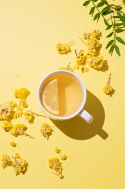 Sarı arka planda beyaz bir fincanda limonlu bitkisel çay. Dokunulmazlık için detoks içeceği konsepti. Üst görünüm ve kopyalama alanı.
