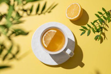 Sarı arka planda beyaz bardakta limonlu bitki çayı. Dokunulmazlık için detoks içeceği konsepti. Üst görünüm ve kopyalama alanı.