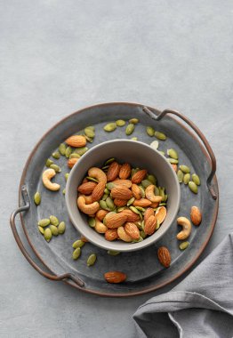 Fındık karışımı. Badem, kaju ve kabak tohumları gri arka planda, peçeteli bir kasede. Sağlıklı enerji atıştırmalığı konsepti. Üst görünüm ve kopyalama alanı.