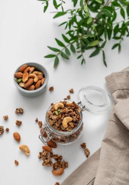 Beyaz arka planda fındıklı ve dallı bir kavanozda ev yapımı granola. Rahatlatıcı yemek. Kahvaltıda sağlıklı ve besleyici tahıl müsli konsepti.. 