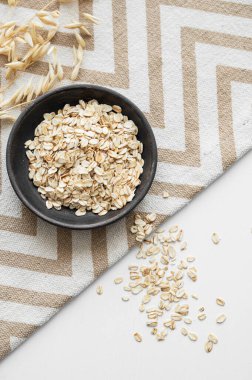 Beyaz desenli arka planda, kuru dallı bir peçetede yulaf ezmesi. Sağlıklı bir kahvaltı hazırlamak için doğal vegan mısır gevreği ürünü konsepti. Üst görünüm ve kopyalama alanı.