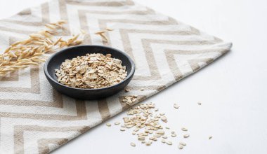 Beyaz desenli arka planda, kuru dallı bir peçetede yulaf ezmesi. Sağlıklı bir kahvaltı hazırlamak için doğal vegan mısır gevreği ürünü konsepti. Boşluğu kopyala.