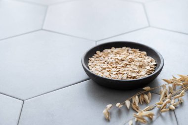 Tahta bir tabakta yulaf ezmesi, kuru dallı gri beton bir fayans üzerinde. Sağlıklı bir kahvaltı hazırlamak için doğal vegan mısır gevreği ürünü konsepti. Boşluğu kopyala.