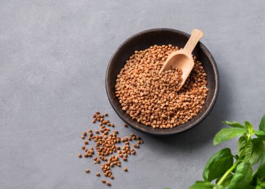 Çiğ karabuğday taneleri, arka plandaki tahta bir kasede taze bitkilerle birlikte. Sağlıklı ve doğal, beslenme ve konforlu gıda kavramı. Üst görünüm ve kopyalama alanı.