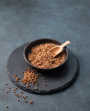 Koyu arkaplanda tahta bir kasede çiğ karabuğday taneleri. Sağlıklı ve doğal, beslenme ve konforlu gıda kavramı. Boşluğu kopyala.