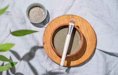 Tabaktaki organik kozmetik mavi kil, gölgesi ve yaprakları olan keten bir arka planda tahta bir tahta üzerinde fırça. Yüz ve vücut için bir maske hazırlama kavramı. Üst görünüm ve kopyalama alanı.