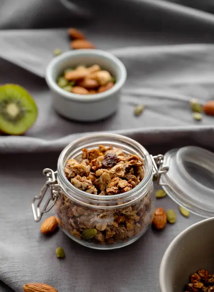 Koyu keten arka planda, fındık ve meyveli kavanozda ev yapımı granola. Kahvaltıda sağlıklı ve besleyici tahıl müsli konsepti.. 