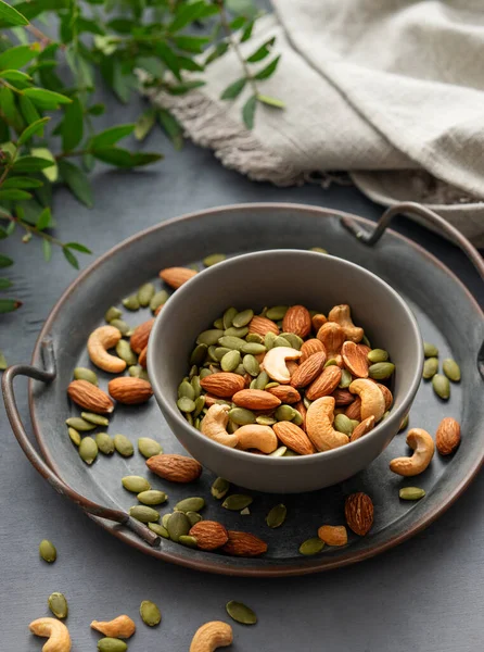 Fındık karışımı. Badem, kaju ve kabak tohumları yeşil dallı koyu bir arka planda bir kasede. Sağlıklı enerji atıştırmalığı konsepti. 