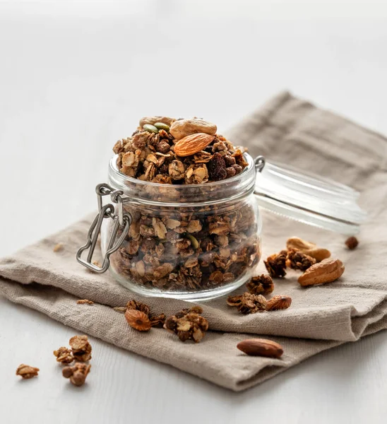Beyaz arka planda fındıklı ve peçeteli kavanozda ev yapımı granola. Rahatlatıcı yemek. Kahvaltıda sağlıklı ve besleyici tahıl müsli konsepti. Ön görünüm.