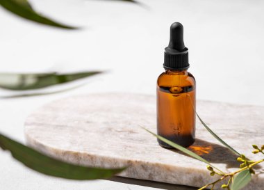 Beyaz arka planda, yaprakları ve gölgesi olan mermer bir tahtanın üzerinde şişedeki yüz ve vücut serumu. Sağlık ve güzellik ürünleri sunumu, satış veya kozmetik reklam afişi için sahne kavramı. 