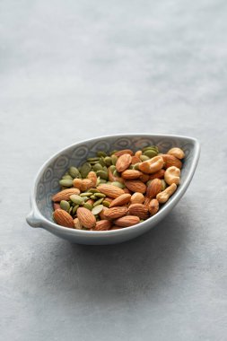 Fındık karışımı. Badem, kaju ve kabak tohumları gri arka planda bir kasede. Sağlıklı enerji atıştırmalığı konsepti. Boşluğu kopyala.