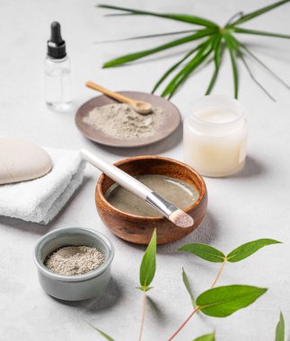 Açık arkaplanda mavi kil, fırça, mum ve palmiye yaprağı olan organik kozmetik ürünler. Ev yapımı cilt bakım ürünleri hazırlama kavramı. 