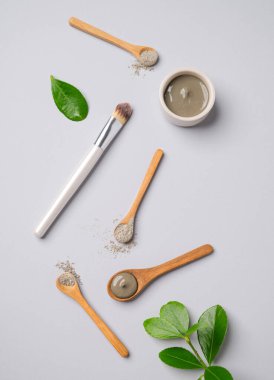 Bir kâse içinde mavi bir kil ve arka planda yaprakları ve fırçası olan kaşıklar düzdü. Ev yapımı cilt bakımı organik kozmetik ürünleri ve spa tedavisi için konsept. Üst görünüm ve kopyalama alanı.