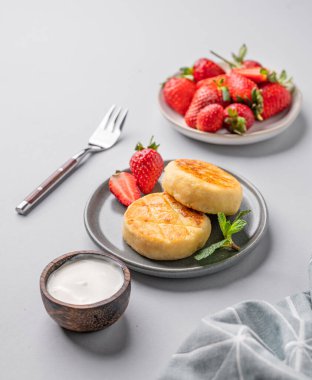 Süzme peynir, peynirli kek ya da çilekli şurup, ekşi krema ve nane yapraklı taze böğürtlen, çatal ve peçeteli gri bir tabakta. Sağlıklı kahvaltı kavramı. 