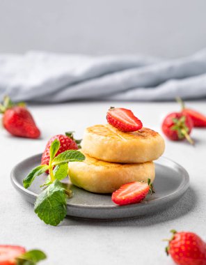 Süzme peynir, cheesecake ya da çilekli şurup ve nane yaprakları açık arkaplanda gri bir tabakta, böğürtlenler yakın. Besleyici ve sağlıklı kahvaltı kavramı. Ön görünüm.