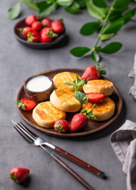 Süzme peynir, cheesecake ya da ekşi kremalı şurup, çilek ve nane yaprakları koyu bir arka planda, peçeteli, çatal bıçaklı ve dallı tahta bir tabakta. Sağlıklı kahvaltı kavramı. 