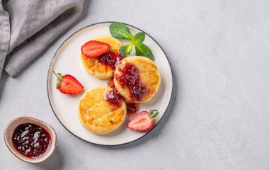 Süzme peynir, peynirli kek ya da beyaz bir tabağa çilek sosu serpiştirilmiş reçelli ve peçeteli çilek. Besleyici ve sağlıklı kahvaltı kavramı. Üst görünüm