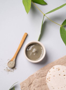 Bir kasede mavi kil ve arka planda hafif bir kaşıkla taş ve peçeteyle. Ev yapımı cilt bakımı organik kozmetik ürünleri ve spa tedavisi için konsept. Üst görünüm.