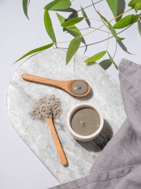 Bir kasede mavi kil ve misket tahtasında kaşıklar, arka planda hafif bir dal ve peçeteyle. Ev yapımı cilt bakımı organik kozmetik ürünleri ve spa tedavisi için konsept. Üst görünüm.