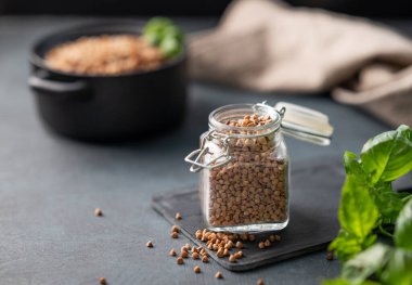 Kavanozda çiğ karabuğday taneleri. Koyu bir arka planda, taze otla birlikte. Sağlıklı ve doğal, beslenme ve konforlu gıda kavramı. Boşluğu kopyala.