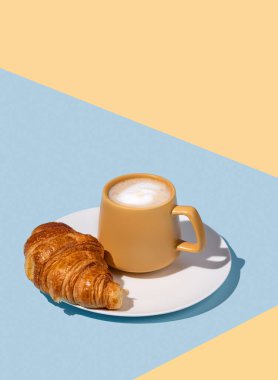 Kahve fincanı ve mavi ve sarı arka planda beyaz bir tabakta taze kruvasan. Yaratıcı tasarım ve sağlıklı yemek ve Fransız kahvaltısı konsepti. Boşluğu kopyala.