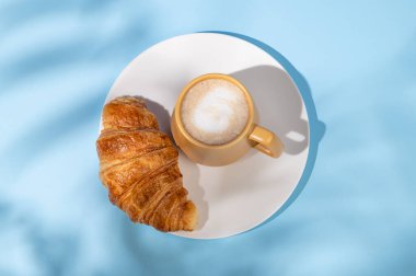 Düz bir kahve fincanı ve beyaz bir tabakta gölgeli taze kruvasan. Yaratıcı tasarım ve sağlıklı yemek ve Fransız kahvaltısı konsepti. Üst görünüm ve kopyalama alanı.