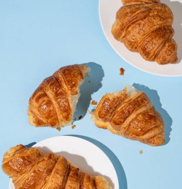 Mavi arka planda gölgeli taze kruvasan yatıyordu. Yaratıcı tasarım ve sağlıklı yemek ve Fransız kahvaltısı konsepti. Üst görünüm. 