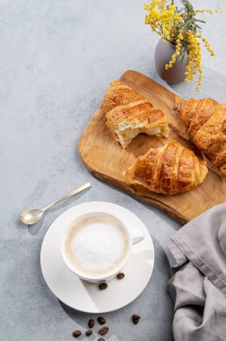 Bir fincan aromatik kapuçino kahve ve kahve çekirdekleri ve çiçeklerle mavi arka planda kesilmiş taze kruvasan. Ev yapımı keklerle lezzetli ve sağlıklı bir kahvaltı.. 
