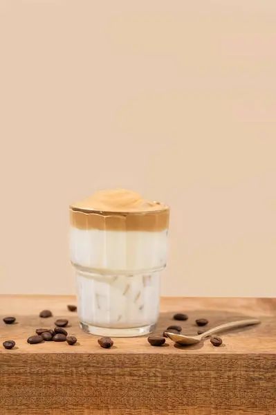 Dalgona coffee. Whipped instant coffee in a glass on a wooden table with coffee beans on a beige background. The concept of a trendy and popular drink. Free space for text.