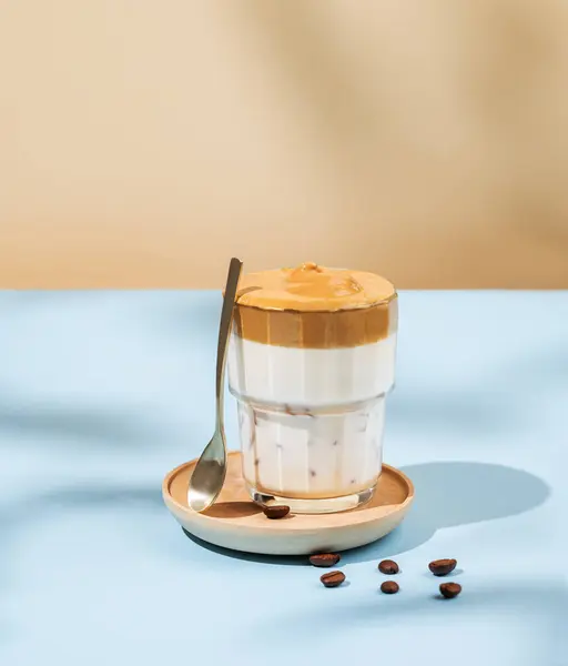 Vegan dalgona coffee. Whipped instant iced coffee with soy milk in a glass on blue background with coffee bean and shadow. The concept of a refreshing trendy and popular healthy drink. Copy space.