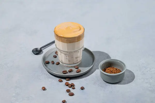 Dalgona coffee. Whipped instant coffee in a glass on a plate with coffee beans on a blue background. The concept of a trendy and popular drink. Free space for text.