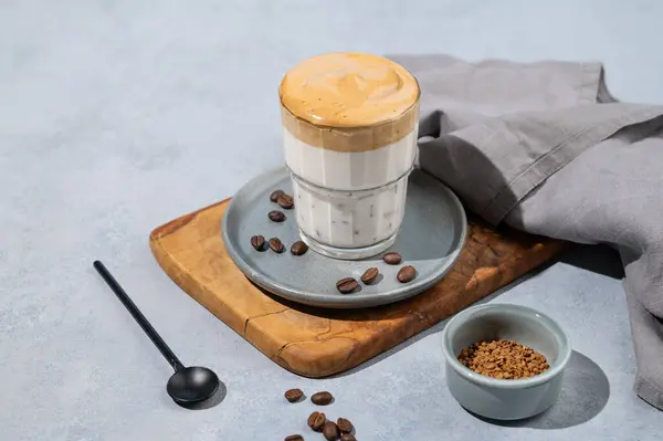 Dalgona coffee. Whipped instant coffee in a glass on a wooden board  with coffee beans on a blue background. The concept of a trendy and popular drink. Free space for text.