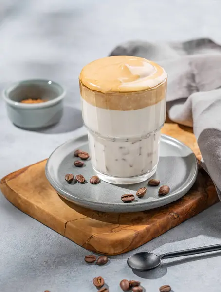 Dalgona coffee. Whipped instant coffee in a glass on a wooden board  with coffee beans on a blue background with morning shadows. The concept of a trendy and popular breakfast drink.