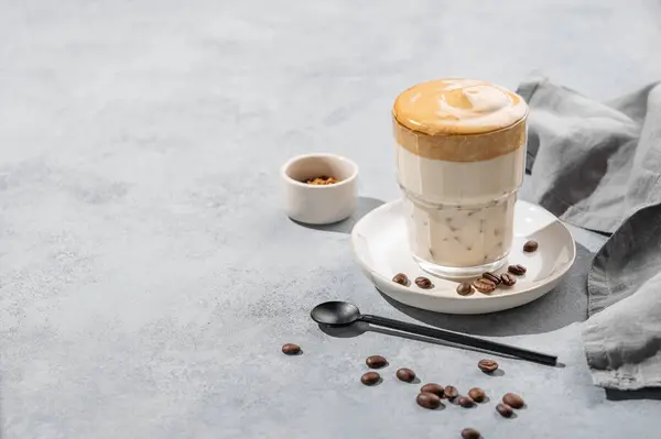 Dalgona coffee. Whipped instant coffee in a glass  with coffee beans on a blue background with napkin. The concept of a trendy and popular drink for breakfast. Free space for text.
