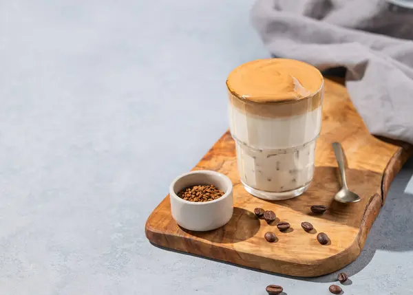 Dalgona coffee. Whipped instant coffee in a glass on a wooden board  with coffee beans on a blue background. The concept of a trendy and popular breakfast drink.  Copy space.