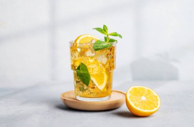 Limonlu buzlu çay, arka planda hafif bir bardakta nane şekeri, gölgeli ve narenciye meyveli. Sıcak bir yaz gününde ferahlatıcı içecek ya da limonata konsepti. Ön görünüm.