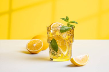 Bir bardak buzlu çay, limonlu ve nane şekerli sarı ve beyaz arka planda, pencerenin gölgesinde. Sıcak bir yaz gününde ferahlatıcı içecek ya da limonata konsepti. 