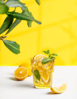 Bir bardak limonlu buzlu çay ve arkaplanda sarı ve beyaz bir arkaplan. Pencere ve dalın gölgesi var. Sıcak bir yaz gününde ferahlatıcı içecek ya da limonata konsepti. 