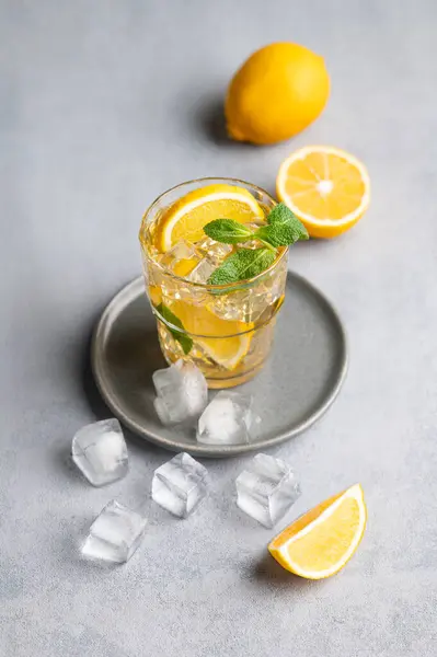 Iced tea with lemon, mint and ice in a glass on a light background with citrus fruits. The concept of a refreshing drink or lemonade on a hot summer day. Top view.