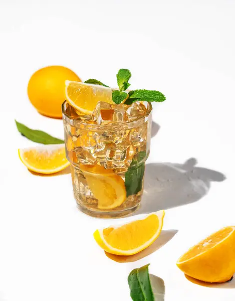 Iced tea with lemon and mint on white background with a shadow and citrus fruits. Trendy concept of a refreshing drink or lemonade on a hot summer day.