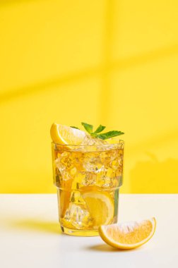 Bir bardak buzlu çay, limonlu ve nane şekerli sarı ve beyaz arka planda, pencerenin gölgesinde. Sıcak bir yaz gününde ferahlatıcı içecek ya da limonata konsepti. 