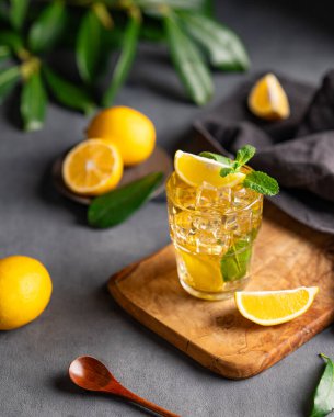 Limonlu ve naneli bir bardak buzlu çay koyu bir arka planda, narenciye ve dallı bir tahta üzerinde. Sıcak bir yaz gününde ferahlatıcı bir içecek ya da limonata konsepti. Üst görünüm.