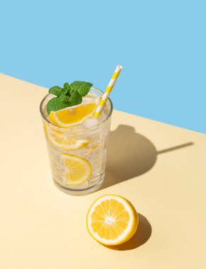 Limonlu, naneli ve buzlu soğuk bir limonata, sarı ve mavi arka planda gölgeli. Ferahlatıcı ve sağlıklı içecek konsepti. 